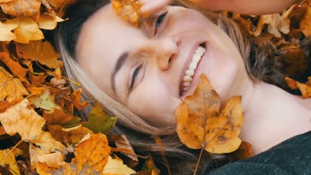 Portret van het gezicht van mooie jonge meisje zonder make-up die ligt in de herfst geel loof en geniet van het leven — Stockvideo