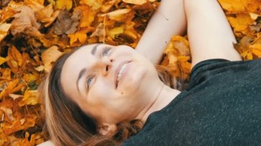 Güzel genç kız sonbahar sarı yapraklar yatıyor ve hayat sahiptir makyaj olmadan yüz portresi. Kuru sonbahar yaprakları gülünecek bir kadının yüzünde düşmek