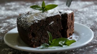 Ev yapımı fırında çikolatalı browni kek beyaz bir tepside pudra şekeri ile boğuk nane yaprakları ile süslenmiş. Dilim kek pasta plaka kapalı çatal tatili