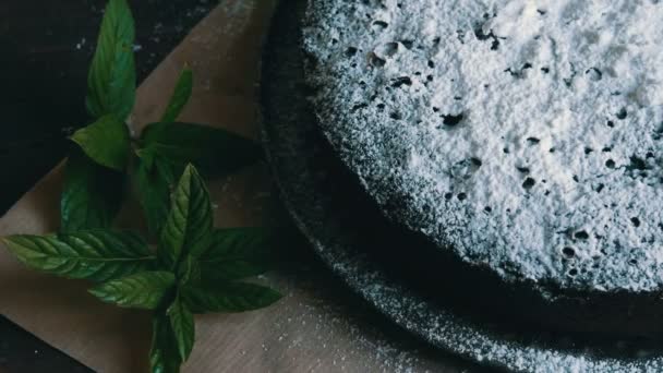 Elegante pastel de chocolate horneado casero generosamente en polvo con un azúcar glaseado junto a hojas de menta fresca — Vídeos de Stock