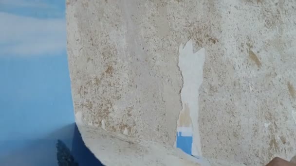 Человек очищает или очищает стену от старых обоев — стоковое видео