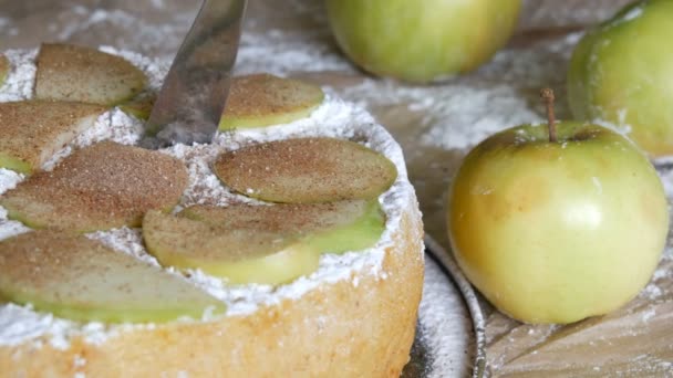 Нож отрезает кусочек вкусного свежеиспеченного пышного яблочного пирога Шарлотта на фоне зеленых яблок. Традиционный домашний яблочный пирог с корицей — стоковое видео