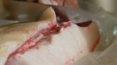Erkek kasap taze domuz eti büyük bir parçası büyük bir bıçakla keser. Domuz yağı ile et ve deri görünümü kapatın