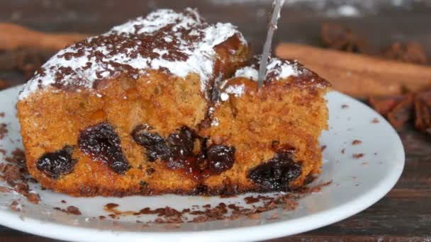 Delicioso pedazo de pastel de cereza recién horneado hecho en casa con azúcar en polvo y chispas de chocolate en un platillo blanco. Un tenedor corta un pedazo de pastel — Vídeos de Stock