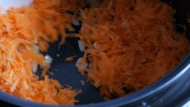 Les carottes et les oignons sont rôtis dans une poêle. Spatule de cuisine blanche agitant les légumes. Alimentation végétarienne — Video