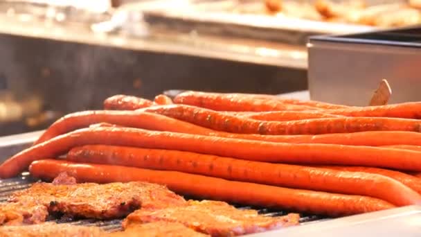 Enorme half-meter lange rode worsten en vlees karbonades met stoom over hen zijn roosteren in kerstmarkt. Traditionele Duitse worsten worden verkocht op de straat op grill — Stockvideo