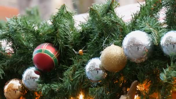 Decoración de Navidad y Año Nuevo en forma de corona de abeto y rojo con bolas de plata y oro de Navidad que cuelgan en una calle y reflejan a las personas que pasan por — Vídeo de stock