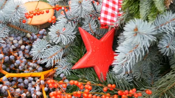 Ασυνήθιστα όμορφη διακόσμηση για τα Χριστούγεννα με τη μορφή μιας ποικιλίας των fir υποκαταστήματα, ένα κόκκινο ξύλινο παιχνίδι με τη μορφή του star και κλαδιά με μούρα. Το πνεύμα των Χριστουγέννων και της Πρωτοχρονιάς — Αρχείο Βίντεο