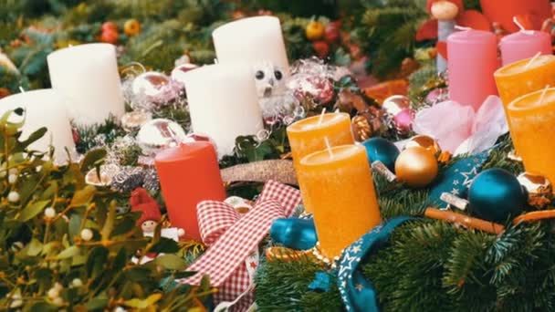 Muchas grandes velas de cera gruesa de Navidad multicolor de pie en acebo y abeto. El espíritu de la Navidad y el año nuevo. Paisaje para unas vacaciones en el mercado en vísperas de Navidad — Vídeos de Stock