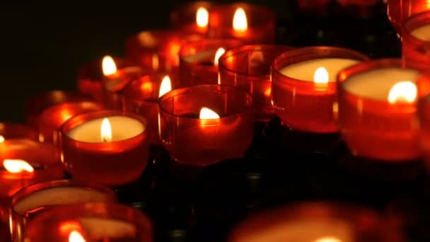 Une rangée de bougies votives rondes rouges de prière chrétienne brûle dans l'obscurité. Lumière de prière Bougies sacrificielles fermer. Brûler des bougies commémoratives dans l'église catholique. Célébration de Noël dans la cathédrale — Video