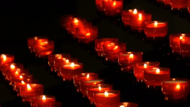 Rij van christelijke gebed rode ronde votief kaarsen branden in het donker. Gebed verlichting opofferende kaarsen. Brandende kaarsen van de memorial in de katholieke kerk. Het vieren van Kerstmis in kathedraal — Stockvideo