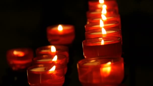 Fila de oración cristiana rojo alrededor de velas votivas arden en la oscuridad. Oración encendiendo velas de sacrificio de cerca. Quemando velas conmemorativas en la iglesia católica. Celebrando la Navidad en la Catedral — Vídeos de Stock
