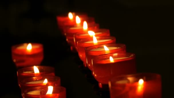 Fila de oración cristiana rojo alrededor de velas votivas arden en la oscuridad. Oración encendiendo velas de sacrificio de cerca. Quemando velas conmemorativas en la iglesia católica. Celebrando la Navidad en la Catedral — Vídeo de stock