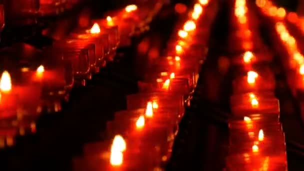 Sorban a keresztény imádság piros kerek fogadalmi gyertya éget a sötétben. Gyertyagyújtás az áldozati imádság zár-megjelöl kilátás. Égő gyertyák memorial a katolikus egyház. Ünneplő karácsony-székesegyház — Stock videók