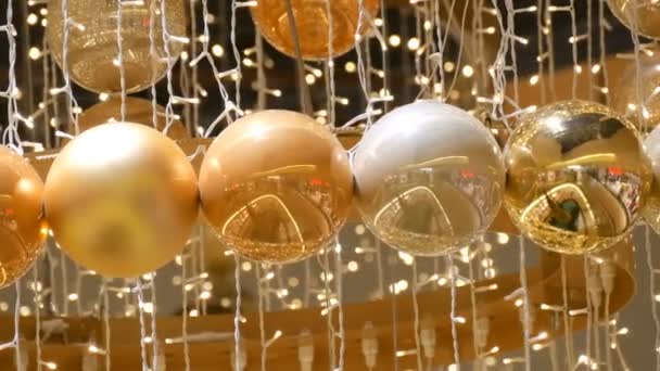 Guld och silver julgranskulor som julpynt i ett köpcentrum. Elegant inredning i köpcentret. Christmas garland med gyllene ljus, i gallerian på nära håll. Suddig lampor. Bokeh. — Stockvideo