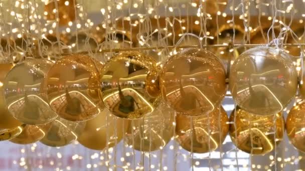 Bolas de oro y plata como decoraciones navideñas en un centro comercial. Elegante decoración en el centro comercial. Guirnalda de Navidad con luces doradas, en el centro comercial de cerca. Luces borrosas. Bokeh. . — Vídeo de stock