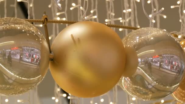 Bolas de oro y plata como decoraciones navideñas en un centro comercial. Elegante decoración en el centro comercial. Guirnalda de Navidad con luces doradas, en el centro comercial de cerca. Luces borrosas. Bokeh. . — Vídeos de Stock