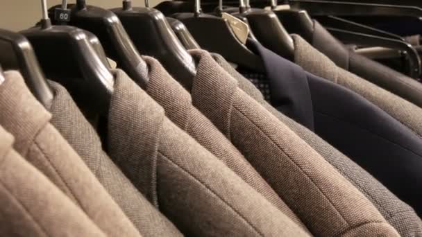 Ряд теплых мужских курток на вешалке в магазине мужской одежды в торговом центре. Различные мужские костюмы висят в торговом центре — стоковое видео