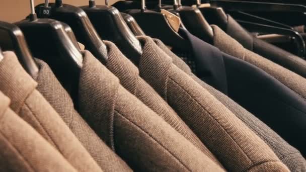 Una fila de chaquetas calientes para hombre en una percha en una tienda de ropa para hombre en el centro comercial. Varios trajes para hombre colgando en el centro comercial — Vídeos de Stock