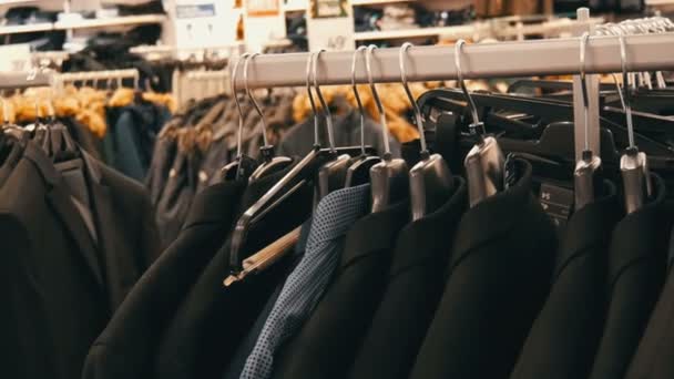 Una fila de chaquetas calientes para hombre en una percha en una tienda de ropa para hombre en el centro comercial. Varios trajes para hombre colgando en el centro comercial — Vídeo de stock