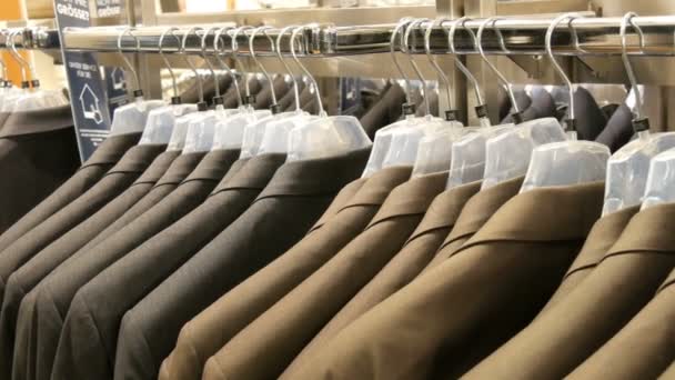 Ruskea ja harmaa miesten takit roikkua ripustimet miesten vaatekauppa ostoskeskuksessa. Valtava valikoima miesten puvut ripustimet ostoskeskuksessa lähikuva — kuvapankkivideo