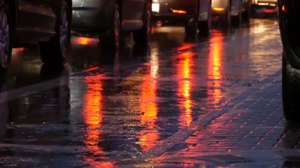 Cars stand in traffic, headlights in rain on asphalt, view below. Rain hits the puddles at night. Reflection of cars lights — Stock Video
