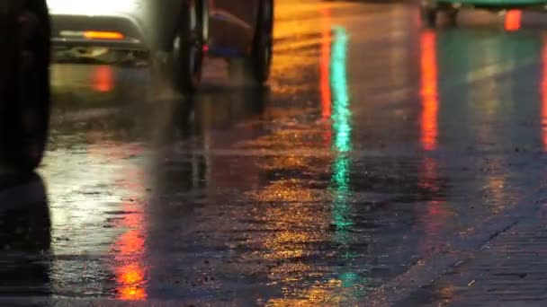 Coches en el tráfico, faros en la lluvia sobre asfalto, vista abajo. La lluvia golpea los charcos por la noche. Reflejo de luces de coches — Vídeo de stock