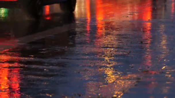 Coches en el tráfico, faros en la lluvia sobre asfalto, vista abajo. La lluvia golpea los charcos por la noche. Reflejo de luces de coches — Vídeo de stock