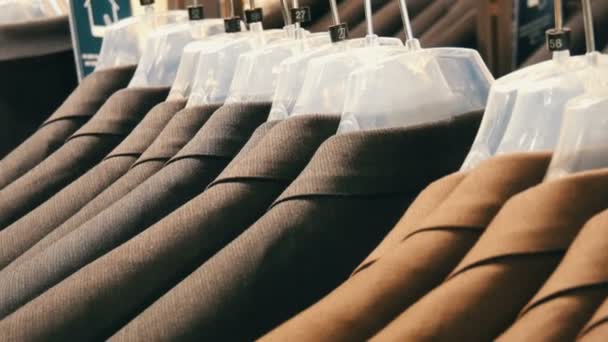 Коричнево-сірі чоловічі куртки повісити на вішалки в магазин одягу чоловіки в торговому центрі. Величезний вибір чоловічі костюми на вішалки в торговий центр крупним планом подання — стокове відео