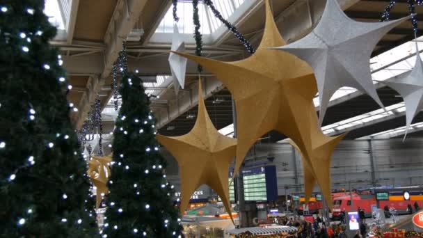 Мюнхен, Германия - 2 декабря 2018 года: Железнодорожный вокзал перед Рождеством. Красиво оформлены для рождественской станции, где люди переполнены. Большие золотые и серебряные рождественские звезды на потолке — стоковое видео