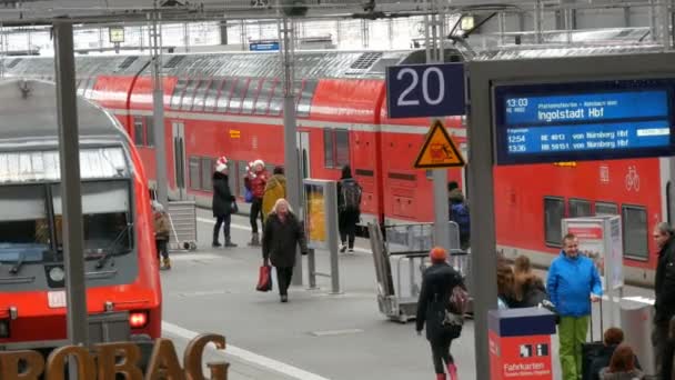 主な鉄道駅でモダンな赤い電車の横にあるプラットフォームに沿ってミュンヘン, ドイツ - 2018 年 12 月 2 日: 観光客乗客歩く — ストック動画