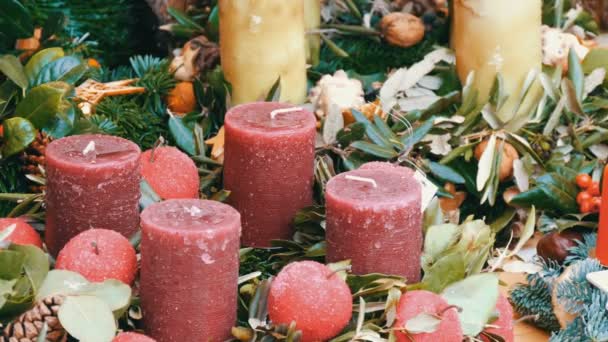 Muchas grandes velas de cera gruesa de Navidad multicolor de pie en acebo y abeto. El espíritu de la Navidad y el año nuevo. Paisaje para unas vacaciones en el mercado en vísperas de Navidad — Vídeos de Stock