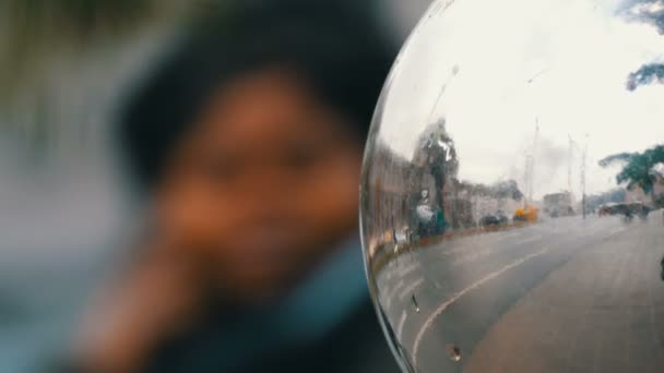 Bonito brinquedo grande árvore de Natal de prata está pendurado na árvore na rua, no reflexo do qual os pedestres e a estrada com carros são visíveis — Vídeo de Stock