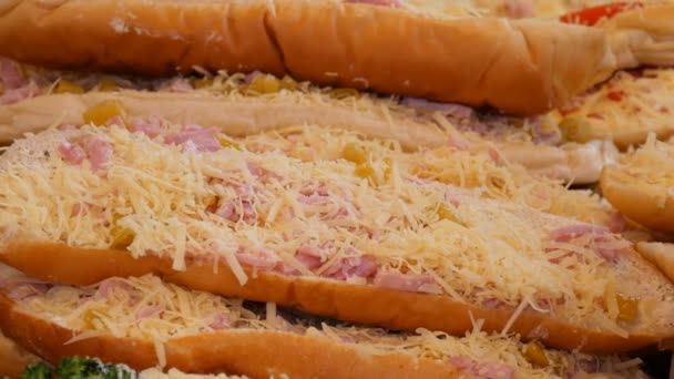 Un énorme morceau de pain sur lequel se trouvent des saucisses, du fromage râpé et des concombres marinés. Grand sandwich sur le comptoir du marché de Noël — Video