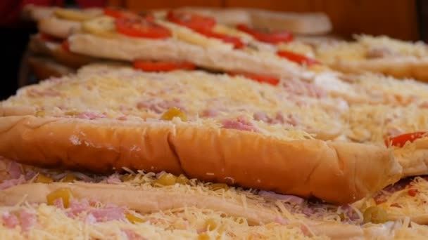 Enorme pezzo di pane in cima al quale è salsiccia, formaggio grattugiato e cetrioli sottaceto. Grande panino sul bancone del mercatino di Natale — Video Stock