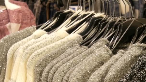 Rij van mooie warme womens fluffy truien van grijs, zwart en wit zijn opknoping op zwarte hangers in de winkel van het winkelcentrum of de mall. Modieuze collectie warme kleren. — Stockvideo