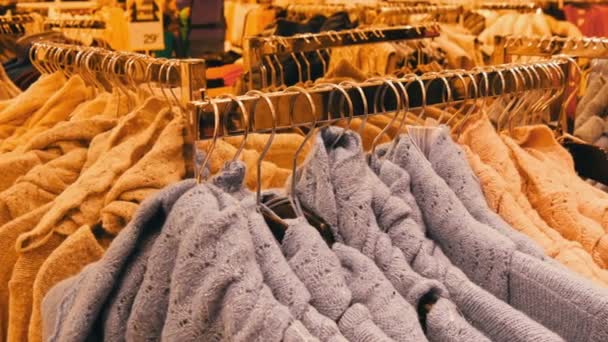 Grande número de novas camisolas elegantes quentes de cores diferentes penduradas em cabides no centro comercial da loja de roupas ou shopping center. Coleção na moda de roupa quente . — Vídeo de Stock