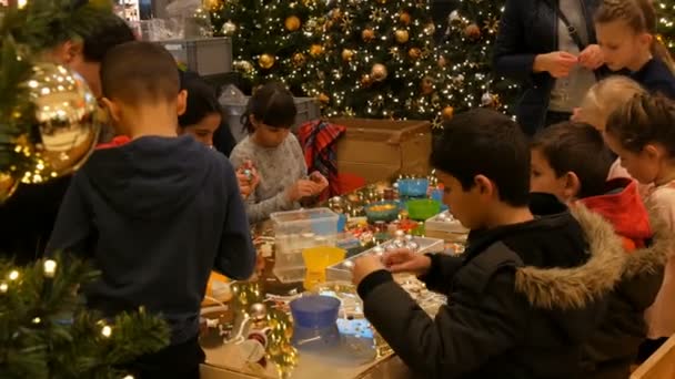 Nuremberg, Duitsland - December 1, 2018: Kinderen krijgen klaar voor kerst en Nieuwjaar maken van handgemaakte ambachten kerstboom speelgoed. Kinderen hebben plezier op mall of shopping center. — Stockvideo