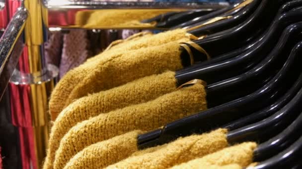 Varios suéteres multicolores de punto con estilo que cuelgan de perchas negras de moda en una tienda de ropa en el centro comercial o centro comercial — Vídeos de Stock