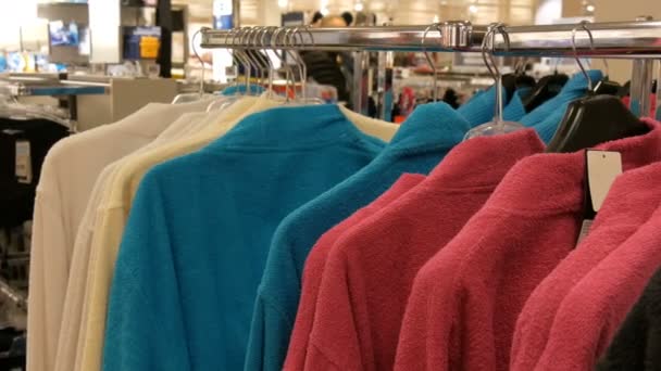 ショッピング センターのお店でハンガーに異なる色とりどりのバスローブの数 — ストック動画