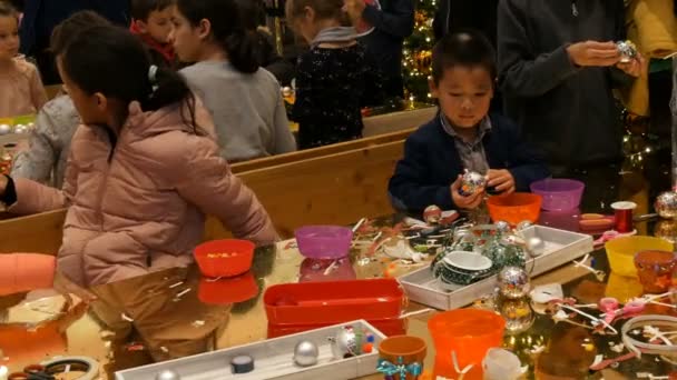 Nuremberg, Alemania - 1 de diciembre de 2018: Los niños se preparan para la Navidad y el Año Nuevo haciendo artesanías juguetes de árbol de Navidad. Los niños se divierten en el centro comercial o centro comercial . — Vídeo de stock