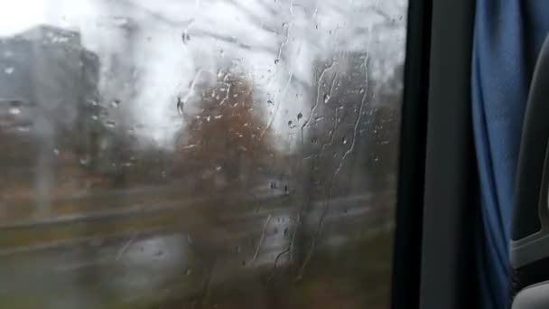 Крупный план дождевых капель и полос на окне движения автобуса по городской улице глубокой осенью — стоковое видео
