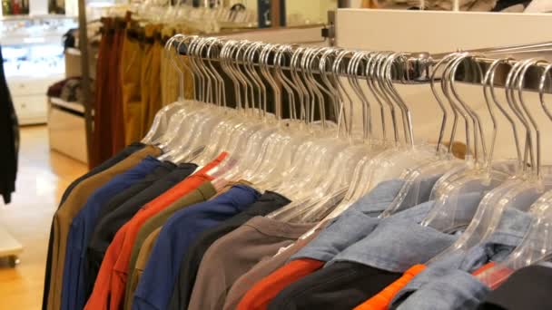 Verschillende multi-gekleurde kleding hangen aan kledinghangers in een kledingwinkel in mall of shopping center — Stockvideo