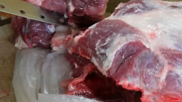 Un gros morceau de porc frais avec du sang et de la viande est coupé en morceaux par un boucher mâle — Video