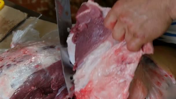 Grande pedaço de porco fresco com sangue e carne é cortado em pedaços por um açougueiro macho. — Vídeo de Stock