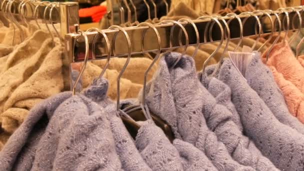 Velký počet nových teplé stylové svetry různých barev, visí na ramínkách v oblečení ukládat nákupní centrum nebo mall. Módní kolekce teplé oblečení. — Stock video