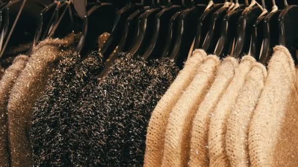 Fila di belle donne calde soffici maglioni di grigio, bianco e nero sono appesi su appendini neri nel negozio del centro commerciale o centro commerciale. Collezione alla moda di vestiti caldi . — Video Stock