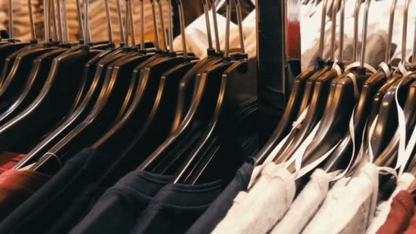 Um grande número de roupas femininas de cores diferentes paira sobre cabides e fica nas prateleiras em uma loja de roupas do centro comercial ou shopping. O problema do consumismo — Vídeo de Stock