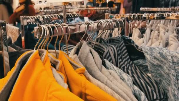 Nuremberg, Alemania - 1 de diciembre de 2018: Un gran número de suéteres de invierno cálidos multicolores cuelgan de las perchas en la tienda del centro comercial, los compradores pasan . — Vídeo de stock