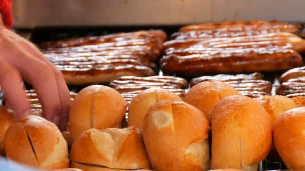 Christmas market, national German sausages are grilled, next to buns. Womens hands turn Nuremberg sausages with help of special tweezers — Stock Video